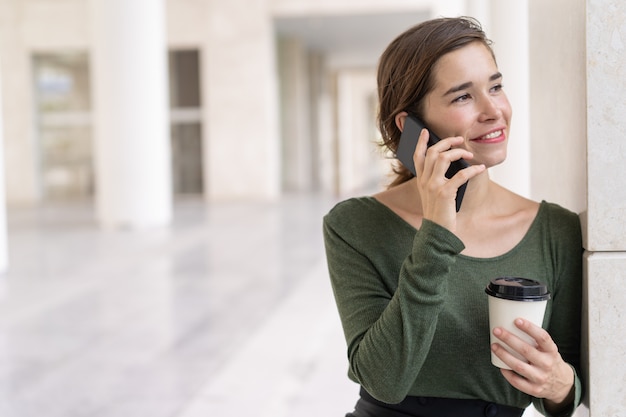 Retrato de mujer sonriente hablando por teléfono móvil en el pasillo