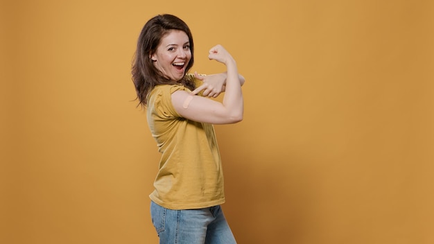 Foto gratuita retrato de una mujer sonriente levantando la manga y mostrando la tirita después de la vacuna contra la gripe o covid flexionando los bíceps del brazo en el estudio. persona orgullosa que revela el vendaje que cubre el lugar de inmunización para la conciencia médica.