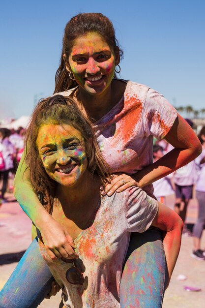 Retrato de una mujer sonriente llevando a su amiga en la espalda celebrando el festival holi