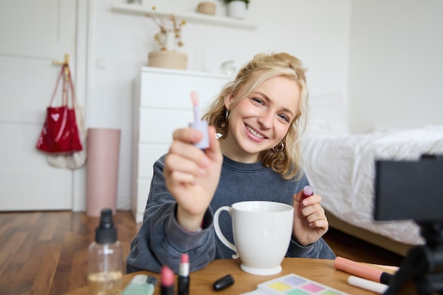 Foto gratuita el retrato de una mujer sonriente muestra brillo labial de maquillaje publicitario en la grabación de su cuenta de redes sociales