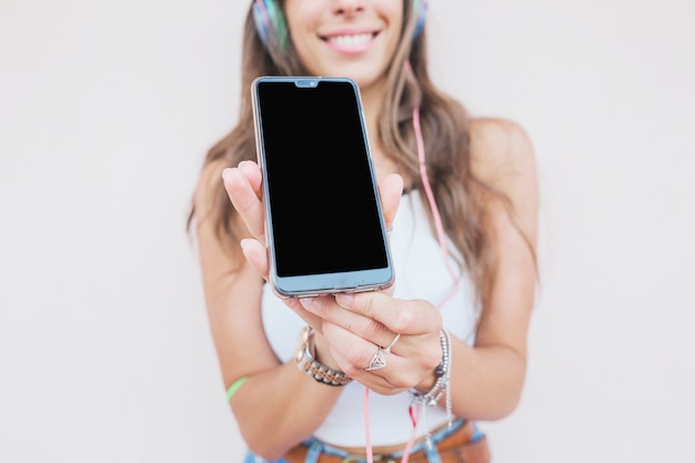 Retrato de la mujer sonriente que muestra la pantalla móvil en el fondo blanco