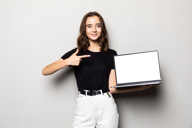 Retrato de una mujer sonriente que señala el dedo en la pantalla de la computadora portátil en blanco sobre gris