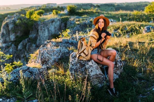 Retrato de una mujer sonriente que sostiene binocular que se sienta en roca