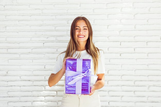 Retrato de una mujer sonriente que sostiene la caja de regalo delante de la pared de ladrillo