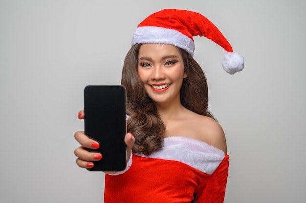 Retrato de mujer sonriente en rojo santa claus mostrando smartphone