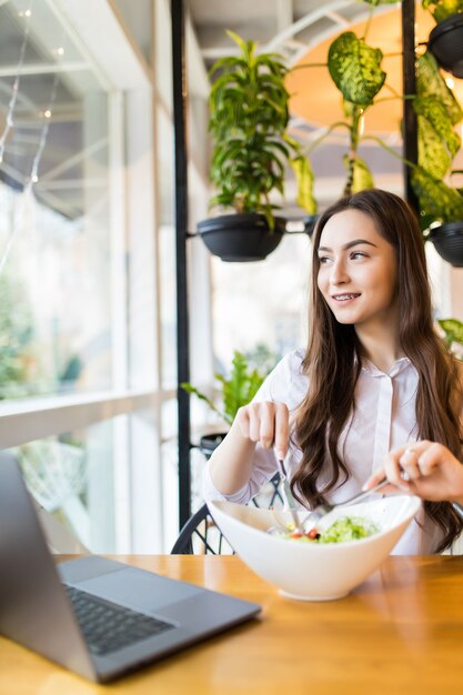 Retrato de mujer sonriente en ropa casual con taza de café y ensalada durante el desayuno en la cafetería.