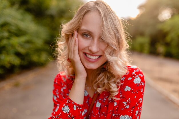 Retrato de mujer sonriente rubia elegante atractiva en traje de moda de verano blusa roja en estilo boho de parque con aretes sonriendo