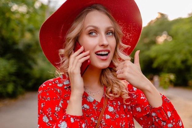 Retrato de mujer sonriente rubia con estilo atractivo con sombrero rojo de paja y blusa traje de moda de verano hablando por teléfono emoción gesto positivo