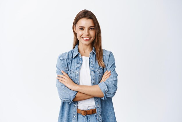 Retrato de una mujer sonriente y segura de sí misma que se siente lista y decidida cruza los brazos en el pecho segura de sí misma mirando a la cámara de pie contra el fondo blanco