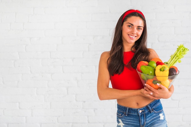 Retrato de mujer sonriente sosteniendo un tazón fresco de frutas y verduras saludables