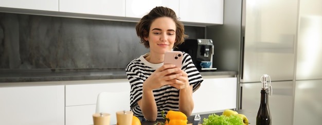 Foto gratuita retrato de una mujer sonriente con un teléfono inteligente en busca de una receta vegetariana saludable de pie cerca