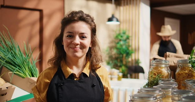 Foto gratuita retrato de una mujer sonriente trabajando en un supermercado sin desperdicio, agregando productos básicos de despensa en los estantes. un comerciante alegre reabastece la tienda de comestibles local con alimentos orgánicos en frascos reutilizables, de cerca