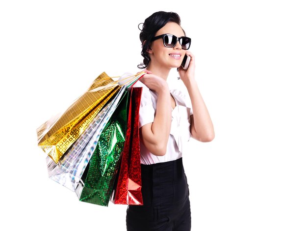 Retrato de mujer sonriente en vasos con bolsas de la compra hablando por teléfono móvil - aislado en blanco.