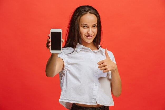 Retrato de una mujer sonriente en vestido rojo que muestra la pantalla del teléfono inteligente en blanco