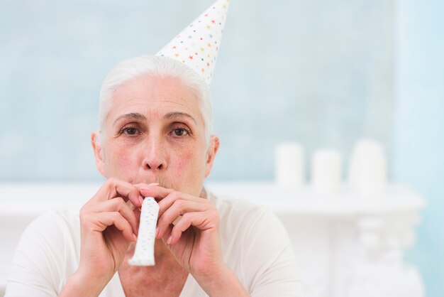 Retrato de mujer soplando fiesta cuerno con sombrero de cumpleaños