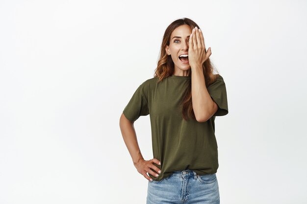 Retrato de mujer sorprendida con un ojo, cubrir la mitad de la cara con la mano y sonriendo emocionada