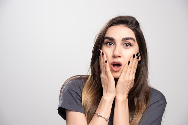 Retrato de mujer sorprendida tocando su rostro posando sobre fondo gris.