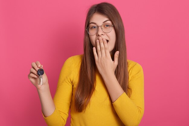 Retrato de mujer sorprendida viste camisa amarilla y anteojos, sosteniendo las llaves en las manos, cubriendo su boca con la mano