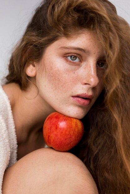 Retrato de mujer sosteniendo una manzana roja entre su cara y rodilla