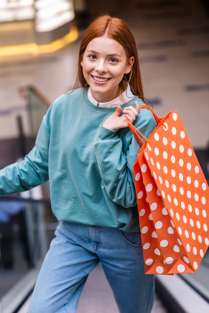 Retrato de mujer subir escaleras mecánicas y sosteniendo la bolsa de compras