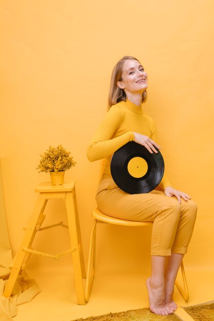 Retrato de mujer sujetando un vinilo en un escenario amarillo