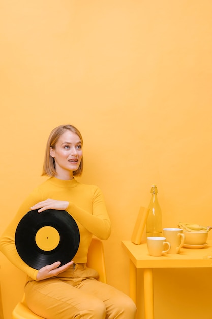 Retrato de mujer sujetando un vinilo en un escenario amarillo