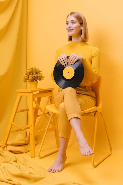 Retrato de mujer sujetando un vinilo en un escenario amarillo