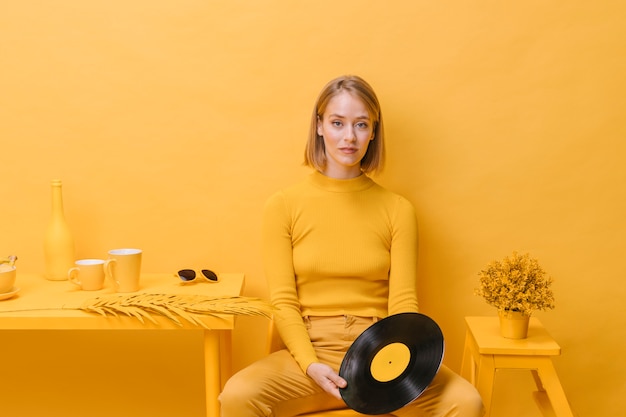 Retrato de mujer sujetando un vinilo en un escenario amarillo