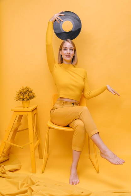Retrato de mujer sujetando un vinilo en un escenario amarillo