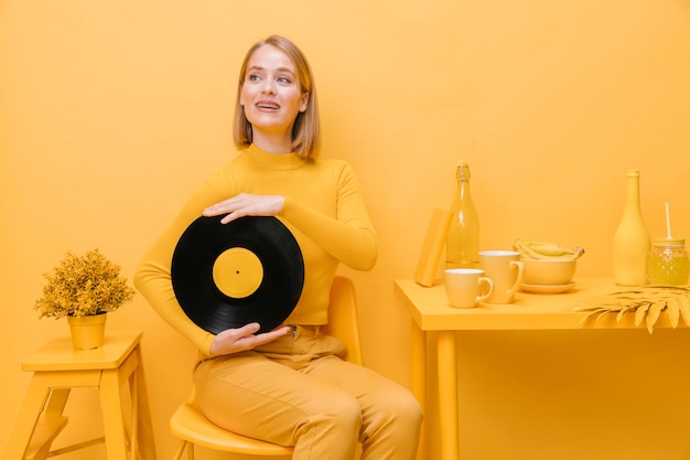 Retrato de mujer sujetando un vinilo en un escenario amarillo