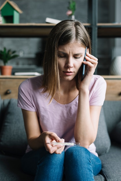 Foto gratuita retrato de una mujer con termómetro hablando por teléfono móvil