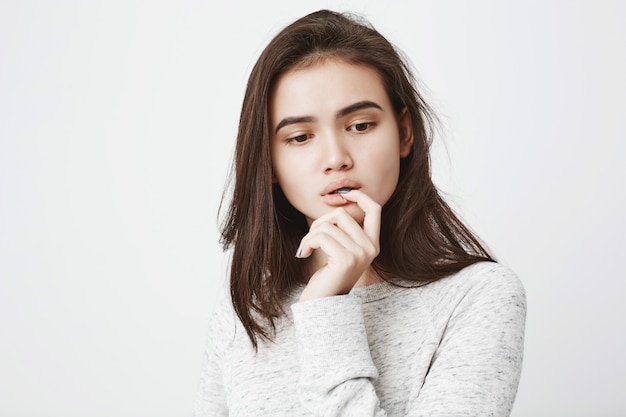 Retrato de mujer tierna soñadora con expresión pensativa, sosteniendo la mano cerca de la boca mientras muerde el dedo y mira hacia abajo