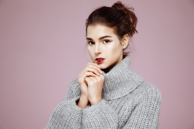 Retrato de mujer tierna en suéter gris calienta las manos en rosa