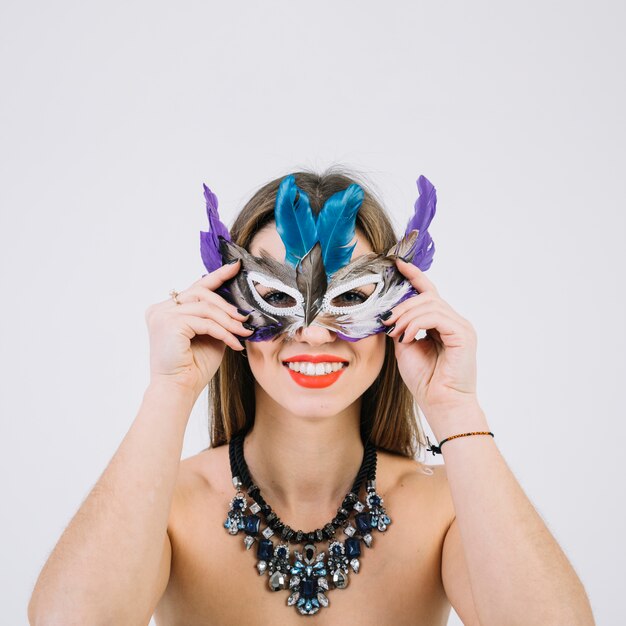 Retrato de una mujer en topless sonriente con máscara de plumas sobre fondo blanco