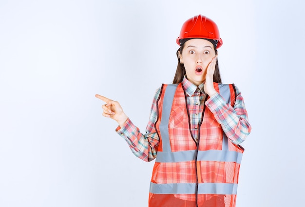 Retrato de mujer trabajador de la construcción apuntando sobre fondo blanco.