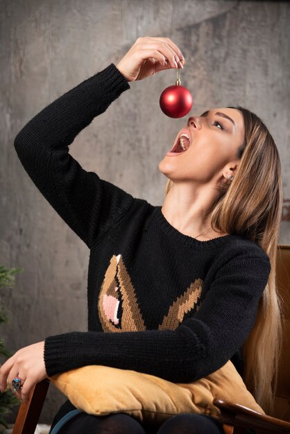 Retrato de mujer tratando de comer bola de Navidad brillante.