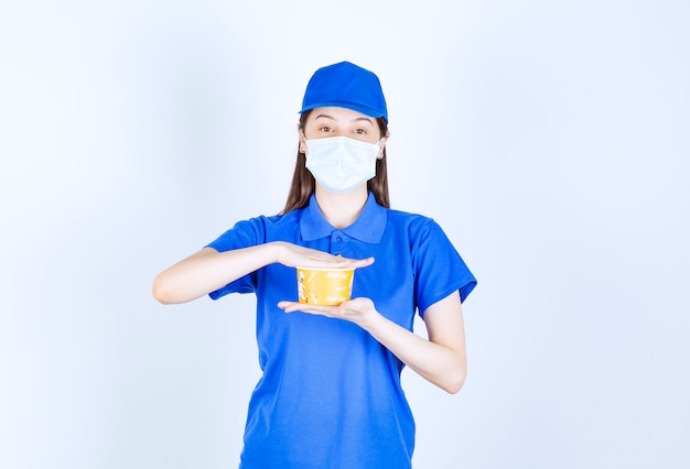 Retrato de mujer en uniforme y máscara médica sosteniendo vaso de plástico