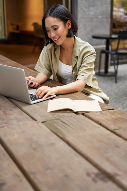 Foto gratuita retrato de mujer urbana con estilo que trabaja en la computadora portátil de un café al aire libre sentado con documentos y compu