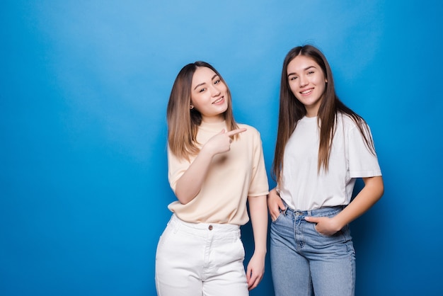 Retrato de mujeres alegres multinacionales en ropa casual sonriendo y apuntando el uno al otro aislado sobre la pared azul