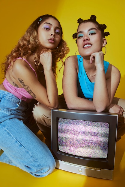 Retrato de mujeres jóvenes en el estilo de moda de la década de 2000 posando con tv