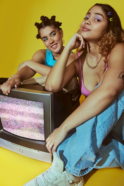 Retrato de mujeres jóvenes en el estilo de moda de la década de 2000 posando con tv