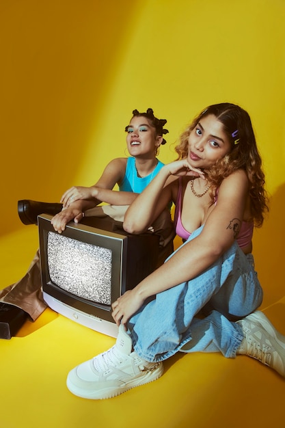 Retrato de mujeres jóvenes en el estilo de moda de la década de 2000 posando con tv