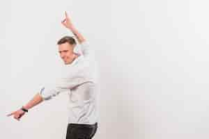 Foto gratuita retrato de una música que escucha feliz del hombre joven en el baile del auricular contra la pared blanca