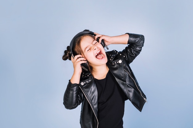 Retrato de una música que escucha de la muchacha en el auricular que ríe contra fondo azul