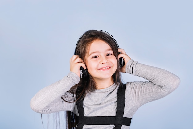 Retrato de una música que escucha de la muchacha feliz en el auricular contra el contexto azul
