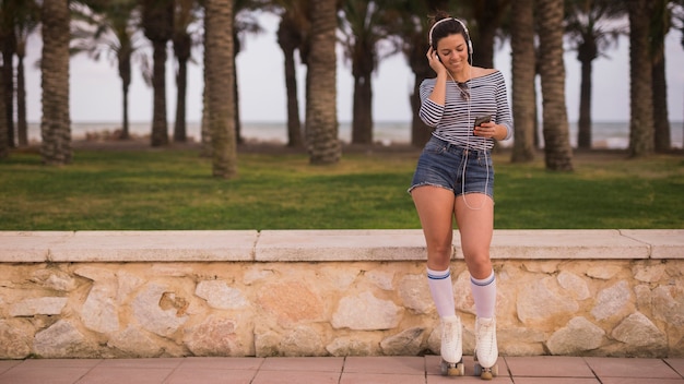 Foto gratuita retrato de una música que escucha del patinador femenino sonriente del rodillo en el auricular