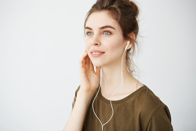 Retrato de la música que escucha sonriente de la mujer hermosa joven en auriculares sobre el fondo blanco.