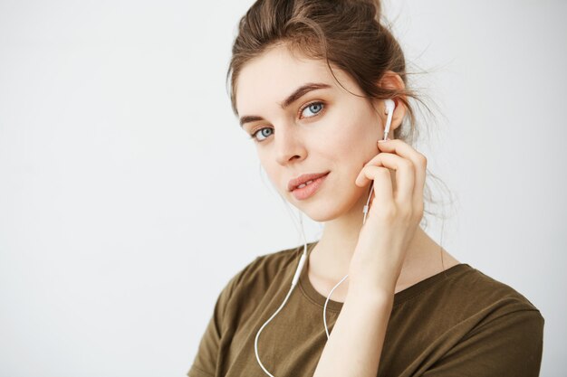 Retrato de la música que escucha sonriente de la mujer hermosa joven en auriculares sobre el fondo blanco.