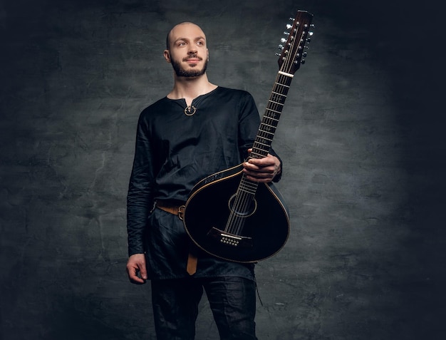 Retrato de un músico de cabeza rapada vestido con ropa celta vieja que sostiene una mandolina vintage.