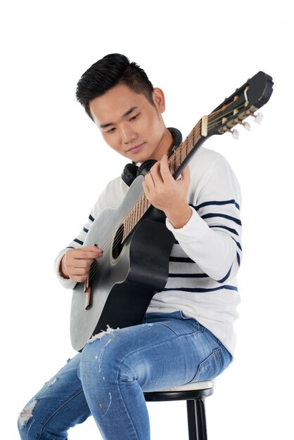 Retrato de músico masculino sentado en un taburete tocando la guitarra